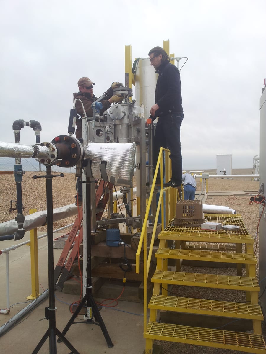 The same test rig seen from further back: the Lynx separator tied into insulated process piping, with a steel walkway, stairs and a ladder beside it.